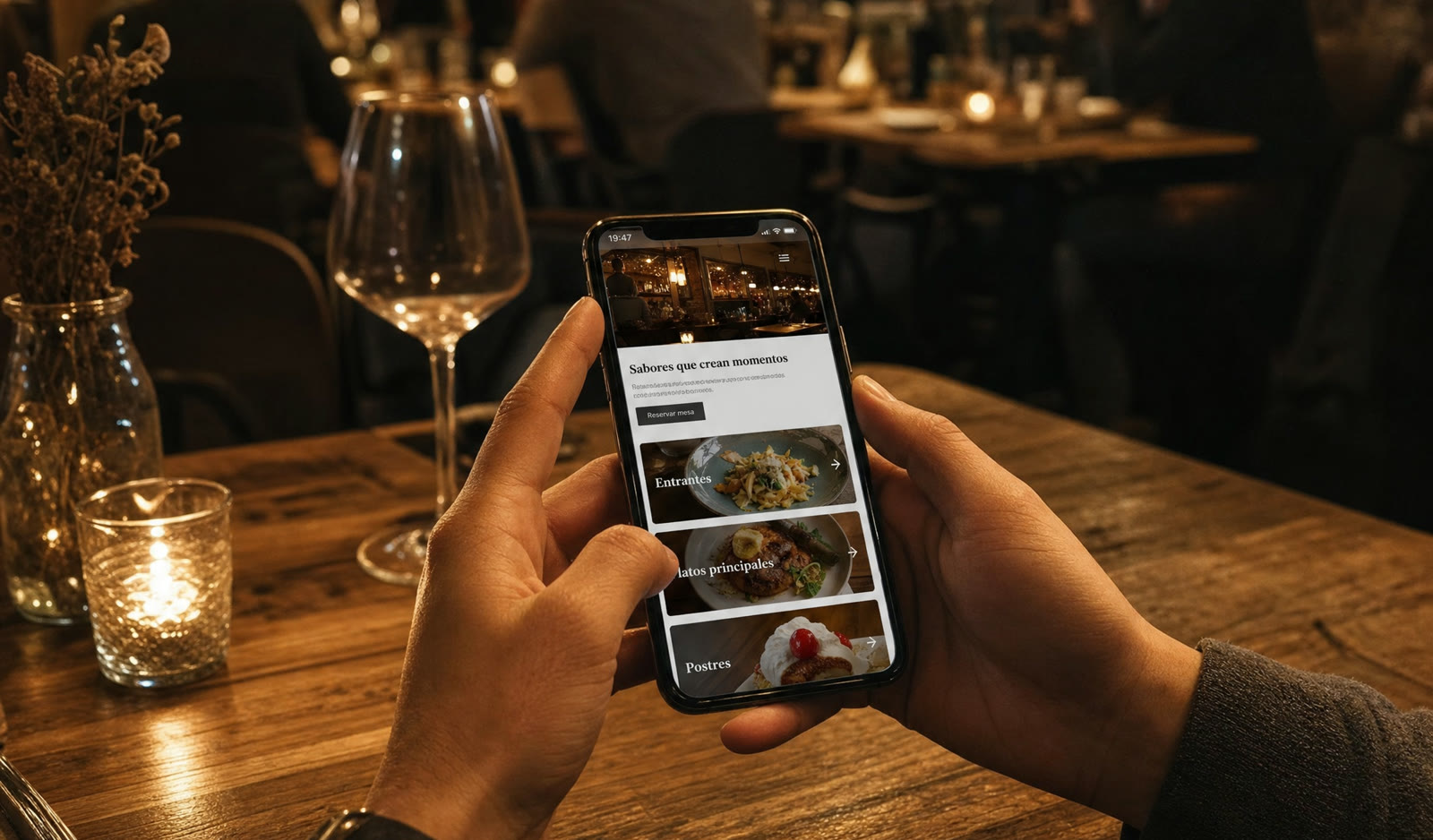 Manos sosteniendo un móvil con la web de un restaurante abierta, sentado a una mesa con luz cálida.